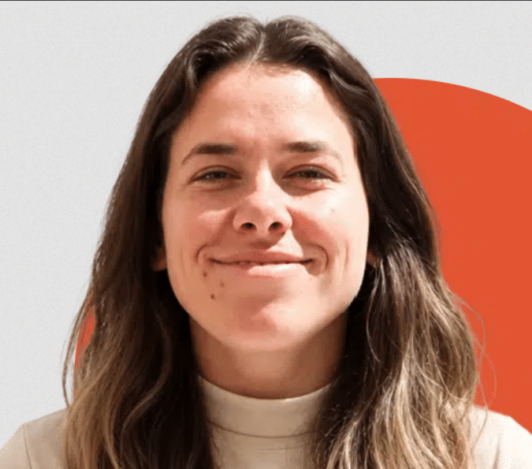 A woman with long brown hair smiling in front of a white and orange background